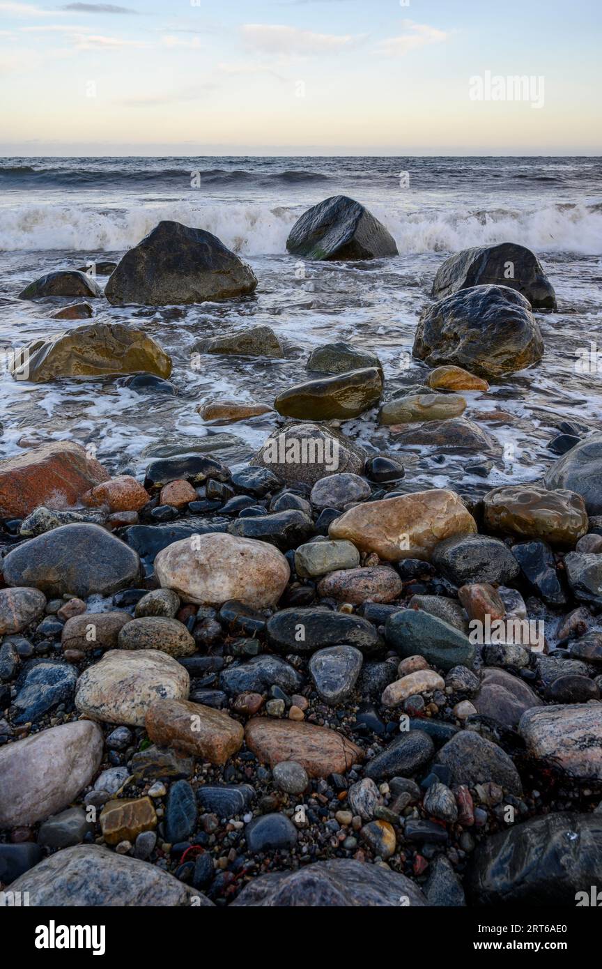 Evening view from the beach on Jomfruland island out to a relatively calm sea with gentle waves breaking and wet, glistening rocks. Telemark, Norway. Stock Photo