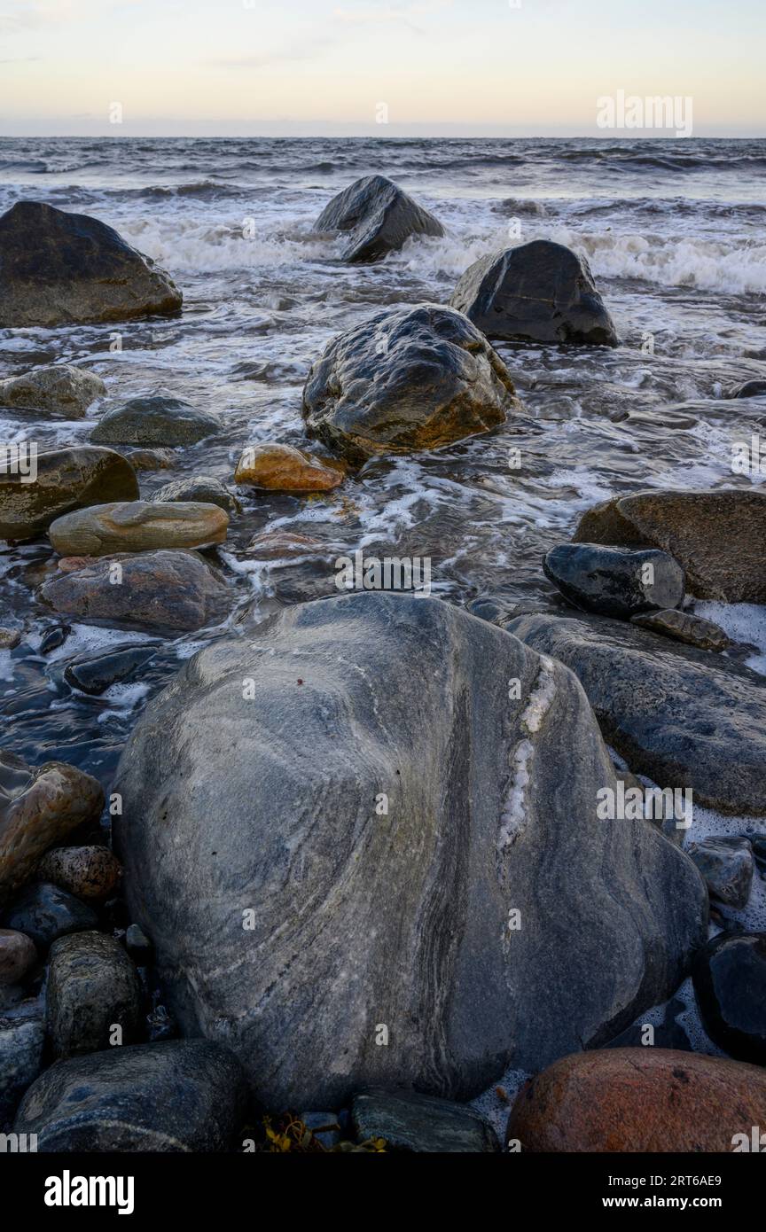 Evening view from the beach on Jomfruland island out to a relatively calm sea with gentle waves breaking and wet, glistening rocks. Telemark, Norway. Stock Photo