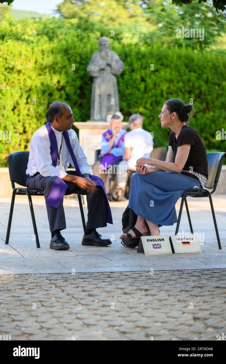 Pilgrims confessing in Medjugorje. Statue of Saint Leopold Mandić – a patron of confessors – is in the background. Stock Photo