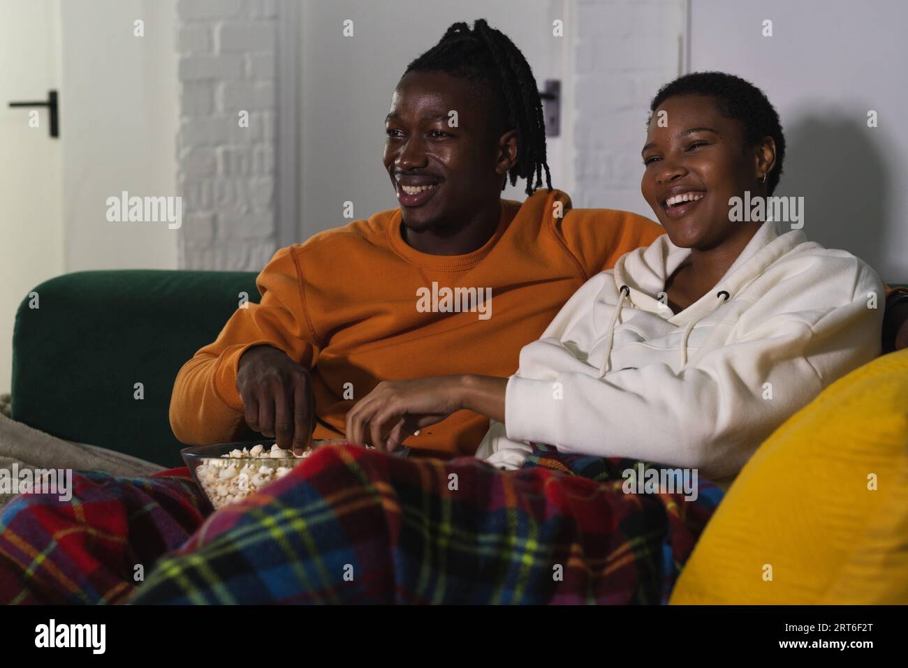 Happy african american couple relaxing at home watching tv and eating ...