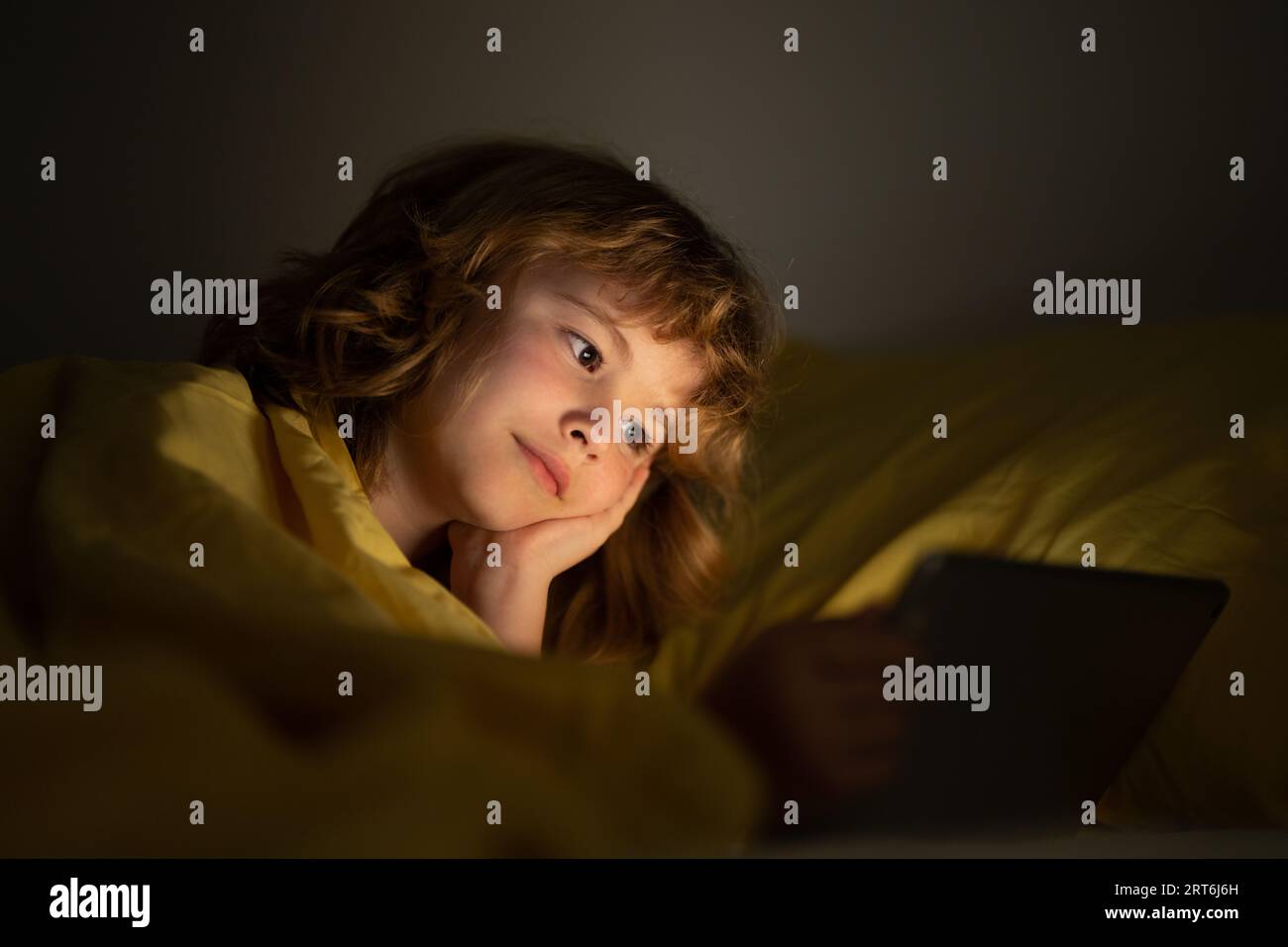 Child in bed under a blanket plays on a tablet in a game in the dark.