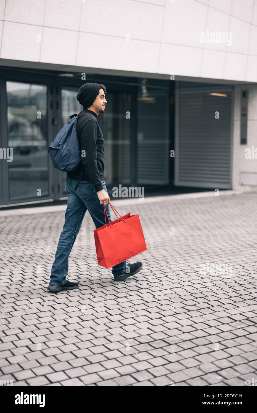 Side view of glad male pedestrian in casual clothes with backpack