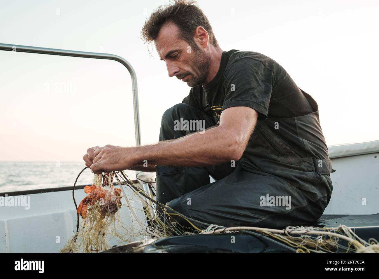 Side view of focused male standing and untangling fishing net on wet ...