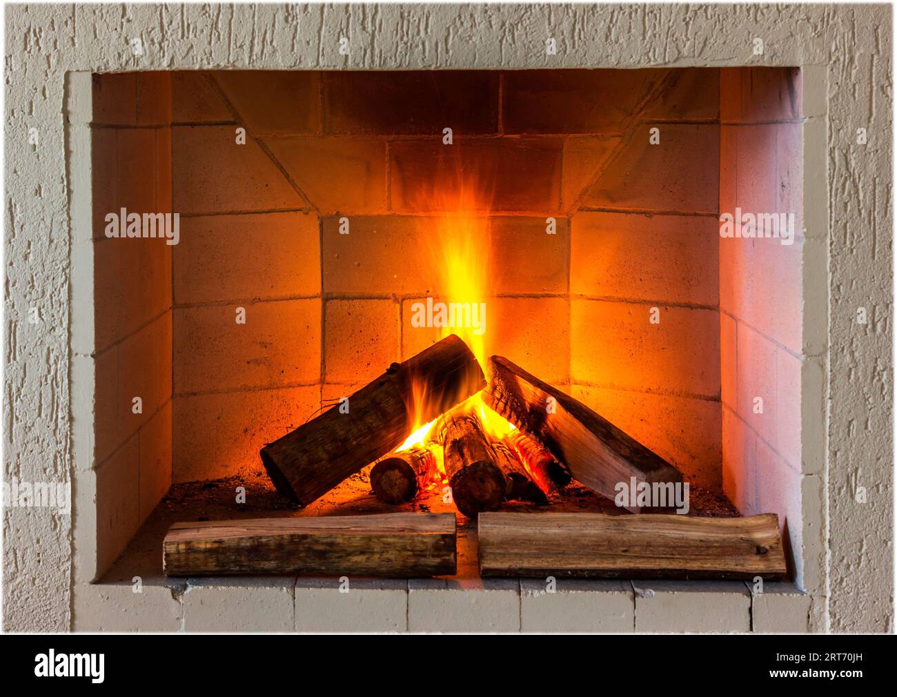 Firewood burning in a cozy brick fireplace featuring a white stone surround Stock Photo