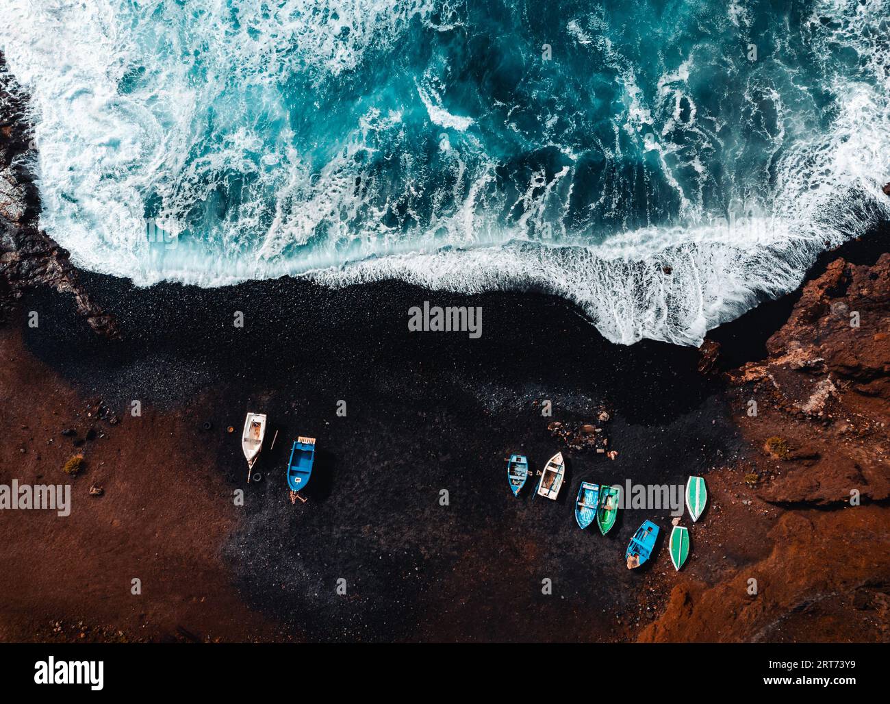 Horizontal aerial photo of black sand volcanic beach with boats on the shore and big and strong waves in ocean -  Lanzarote, Canary Islands. Waves in Stock Photo