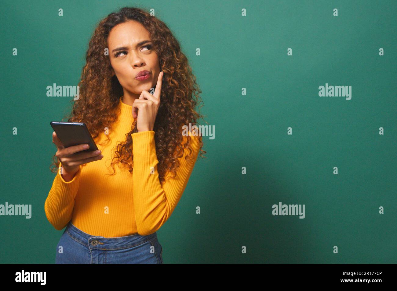 Serious young woman taps chin while thinking, contemplating, green studio Stock Photo