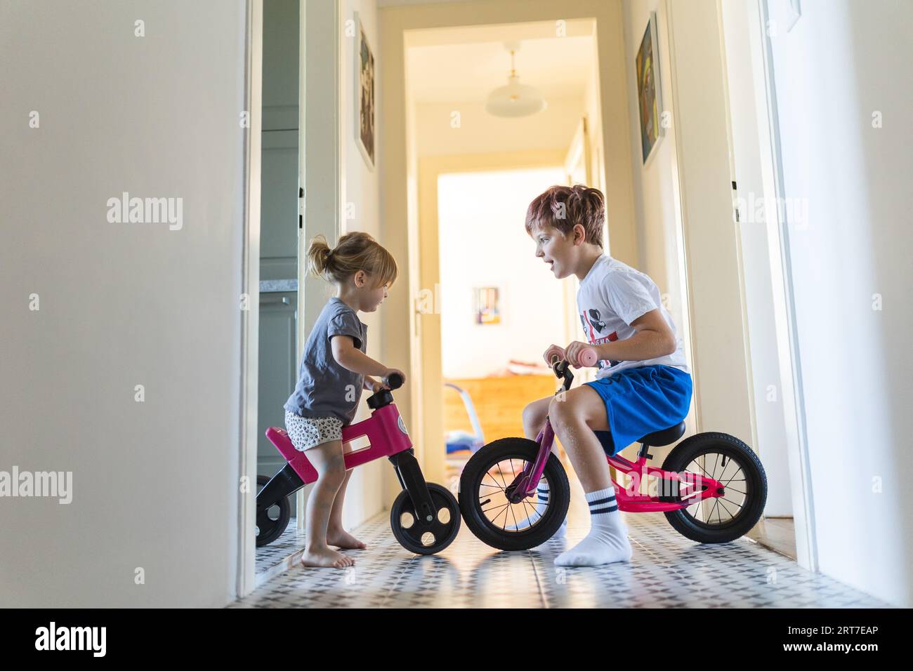 Siblings are riding bicycles indoors in the hallway of the house Stock Photo Alamy