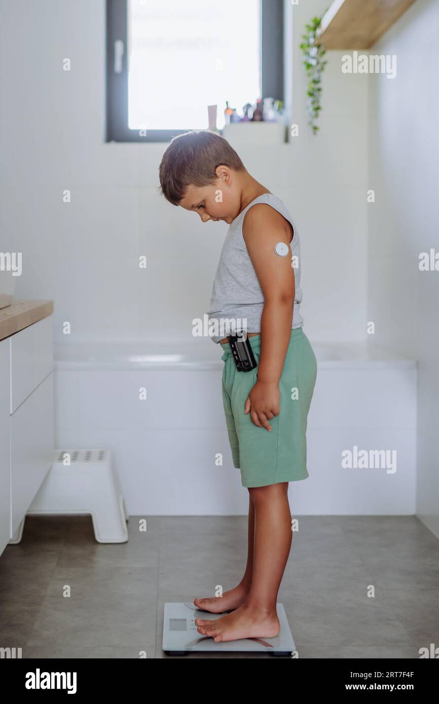 A young boy with diabetes weighing himself on bathroom scale Stock