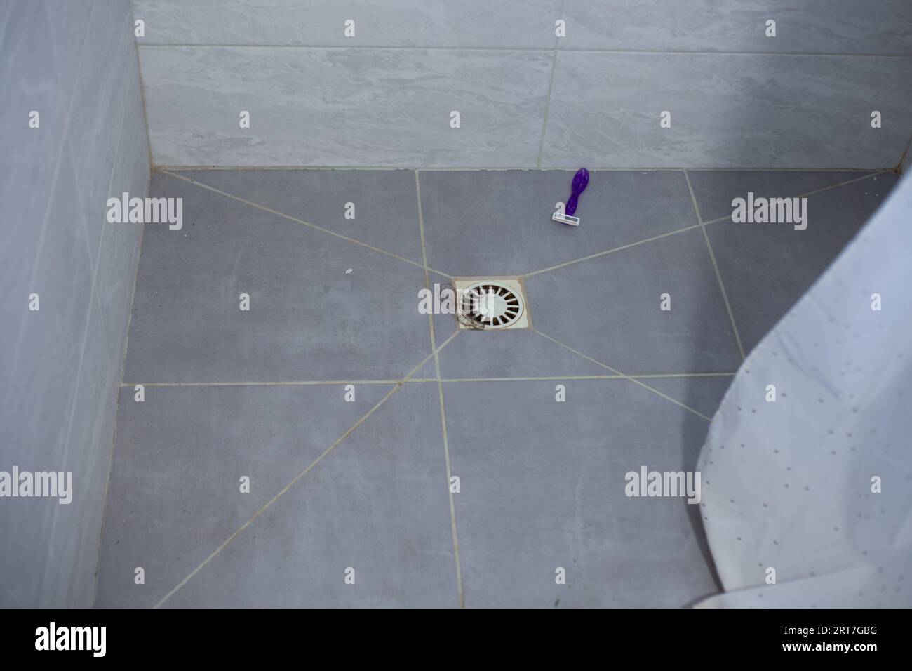 Hair in the shower sink and razor on the floor. Clogged sink after hair