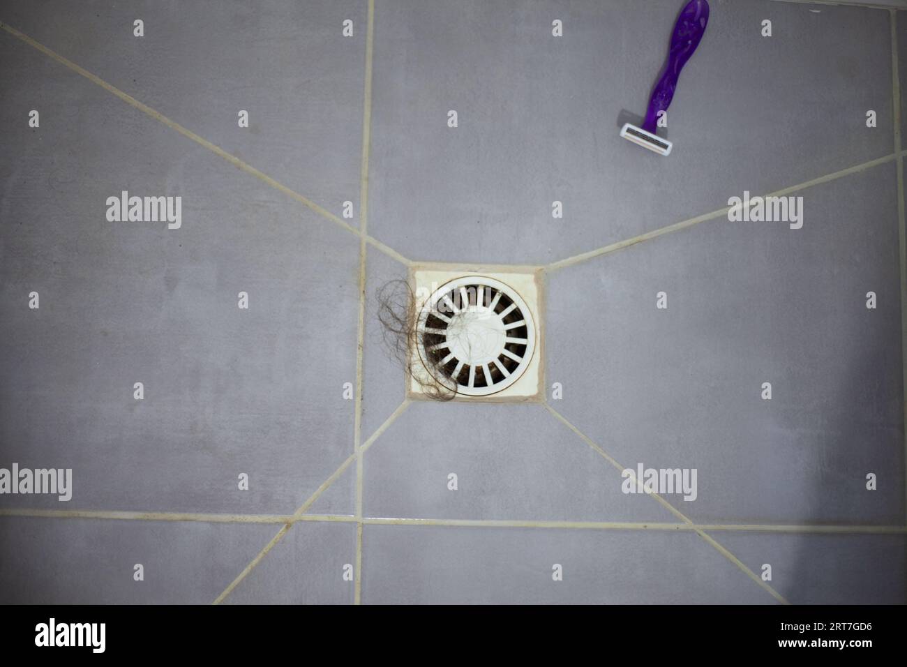 Sink in the shower floor with hair and razor, clogging the drain sink