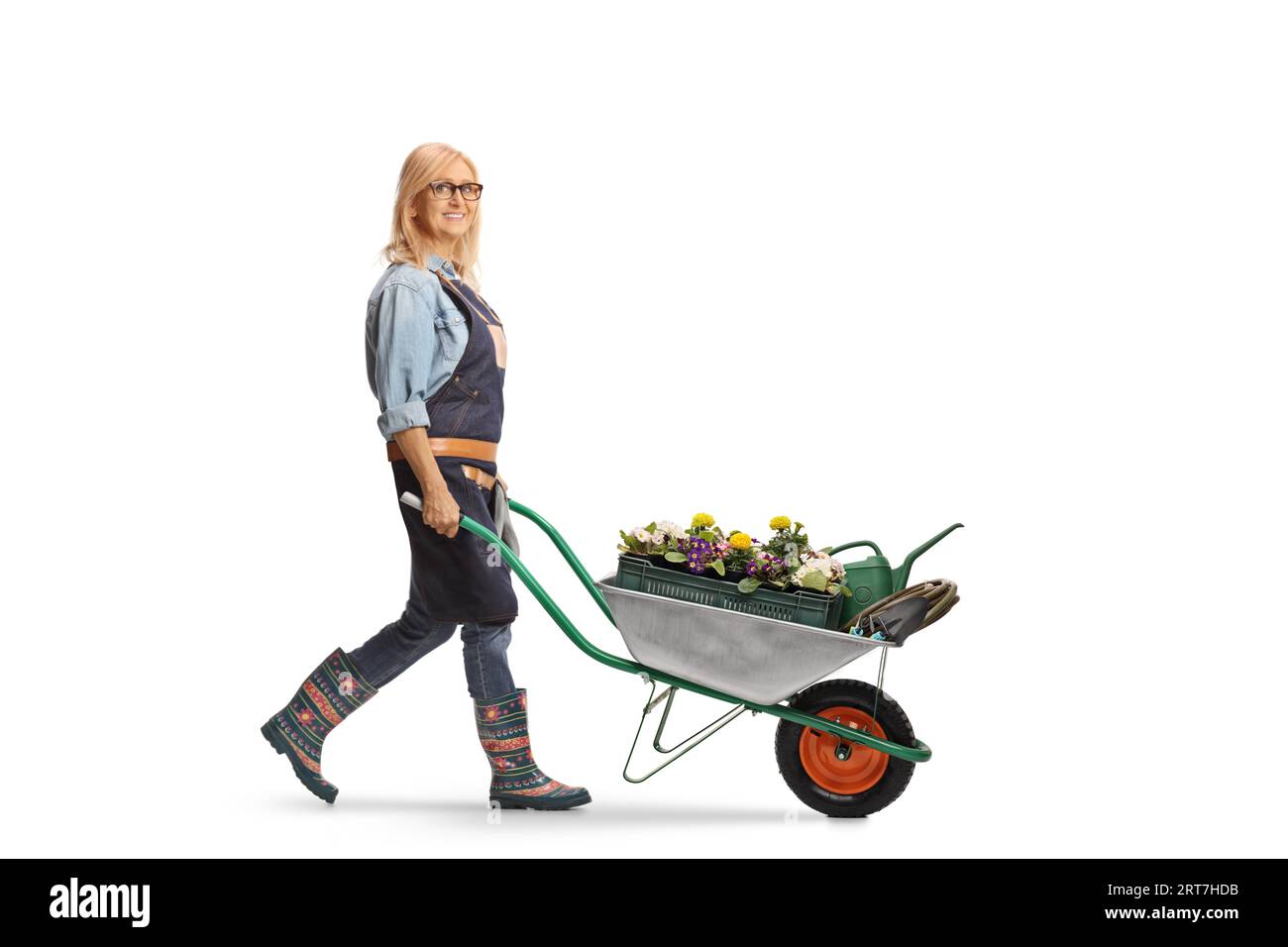 Full length profile shot of a female gardener pushing a wheelbarrow full of flowers solated on white background Stock Photo