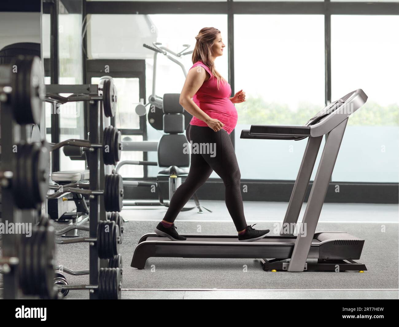 Full length profile shot of a pregnant woman running on a treadmill at