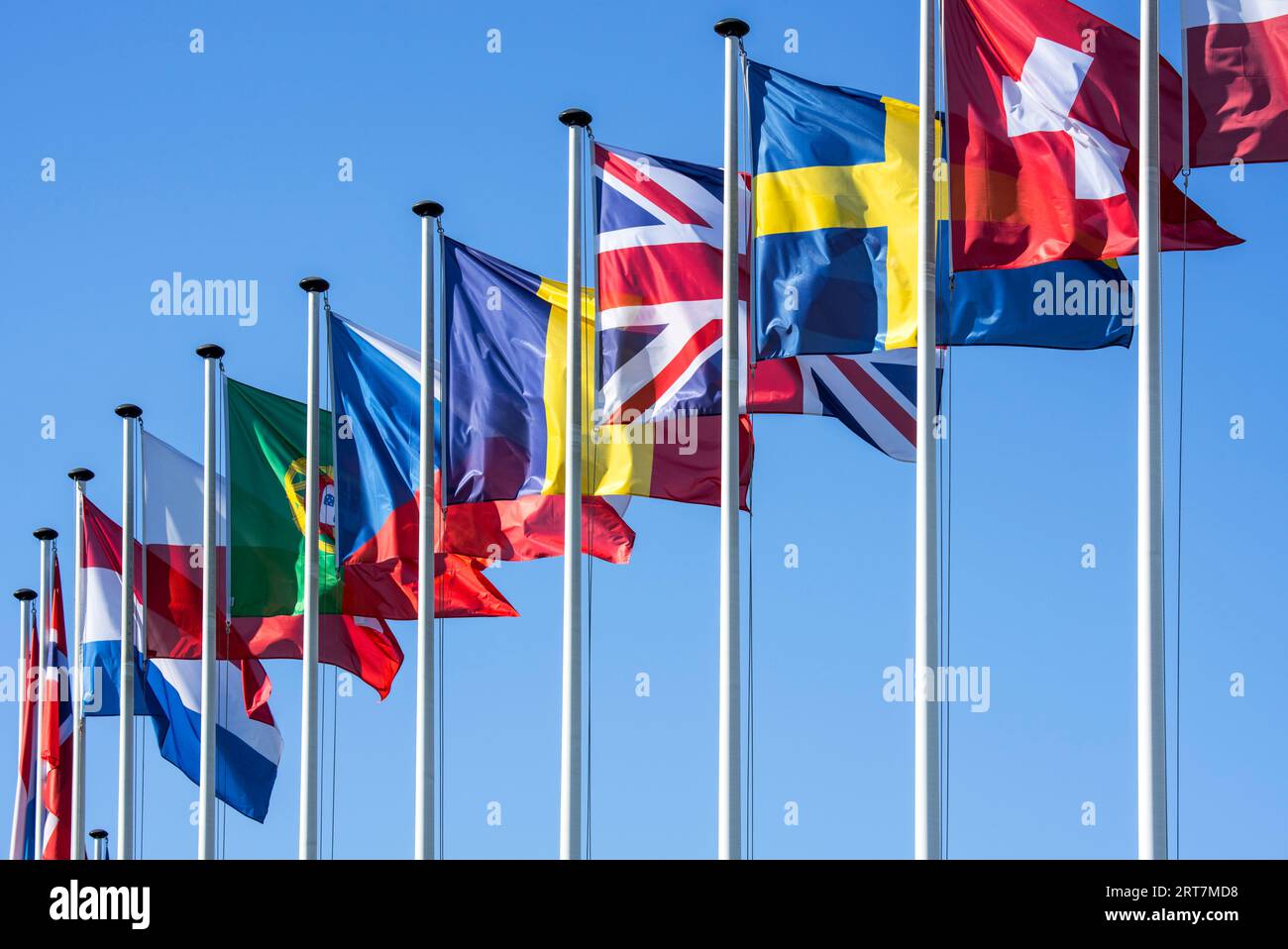 Flags of European countries on flagpoles flying in the wind against blue sky Stock Photo