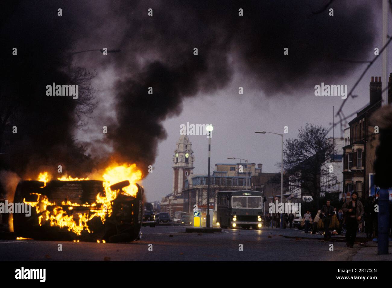 Brixton Riots 1981 UK.  Hijacked burning car set on fire by the rioters. Brixton town hall clock tower in background. Brixton South London Uk April 1980s  England HOMER SYKES. Stock Photo