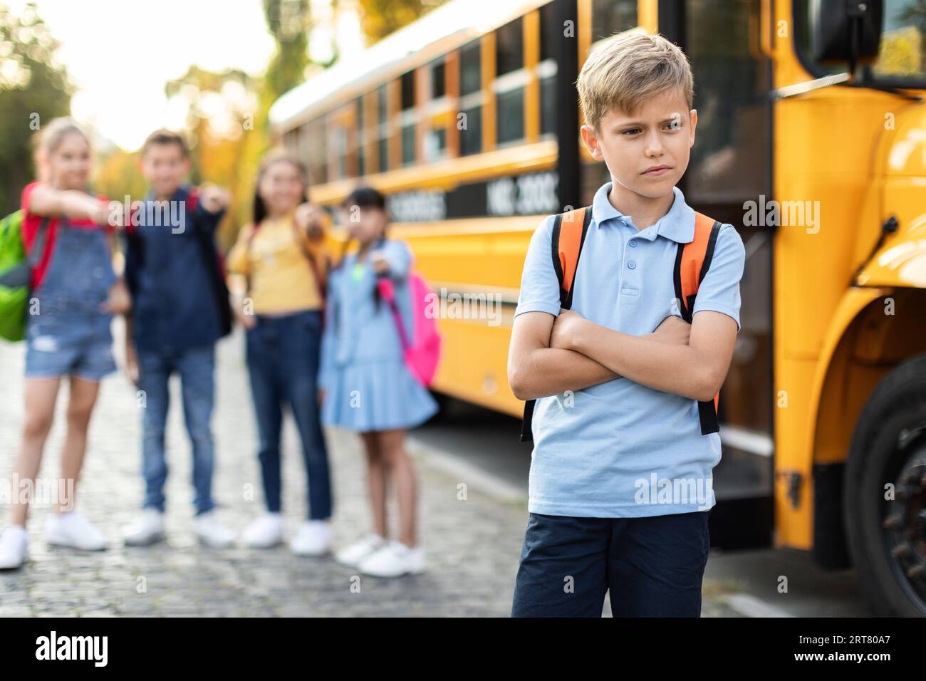 Schoolkids bullying their upset classmate while standing near school bus Stock Photo