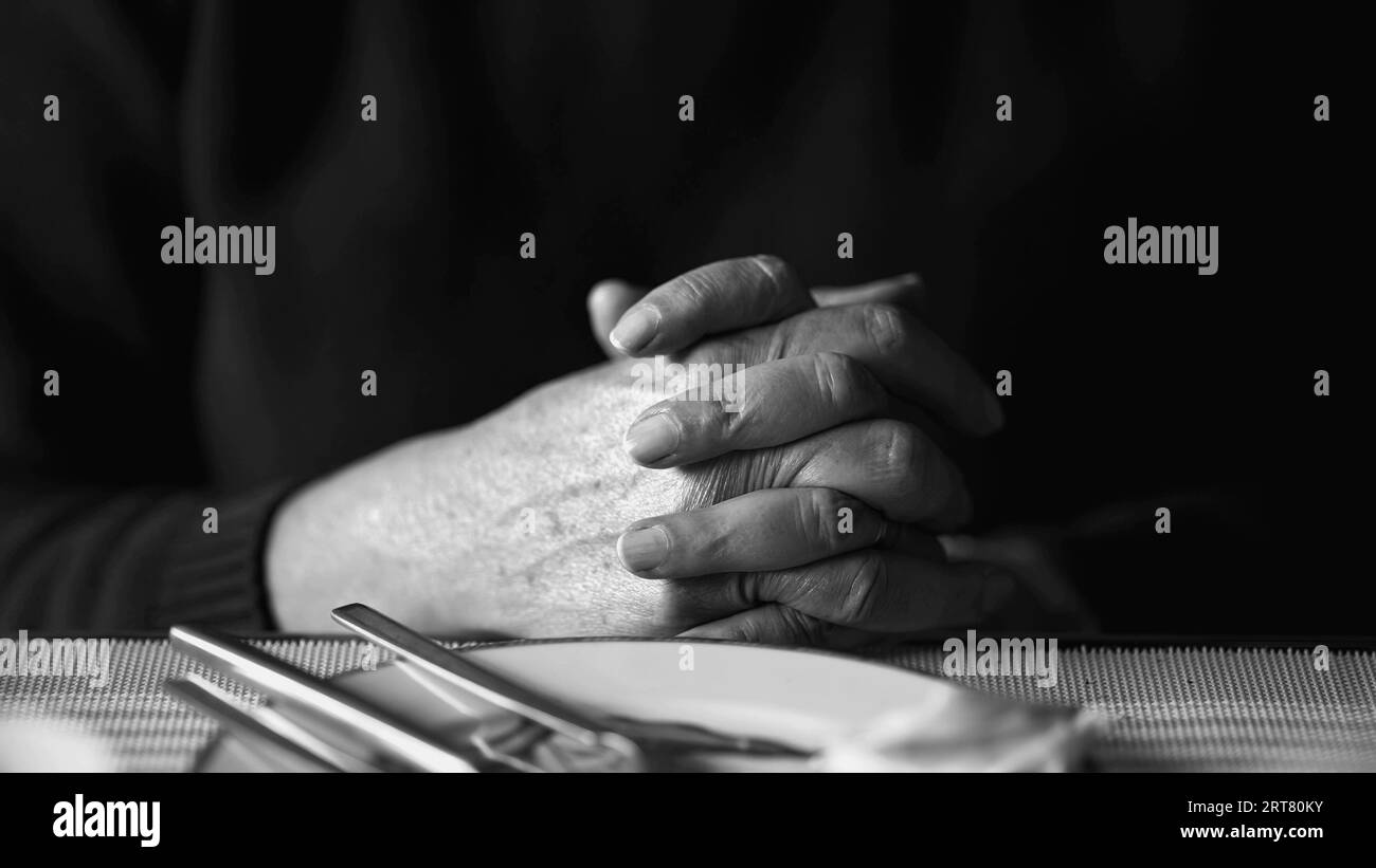 Detailed view of aged hands clasped together, revealing a profound moment of internal pondering and contemplation in monochromatic, black and white Stock Photo