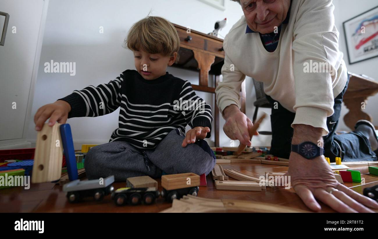Grandfather putting train piece into wooden track, bonding family ...