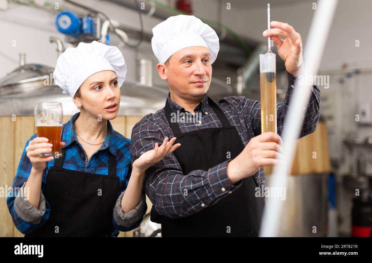 Man and woman brewmasters measuring beer with alcoholometer Stock Photo