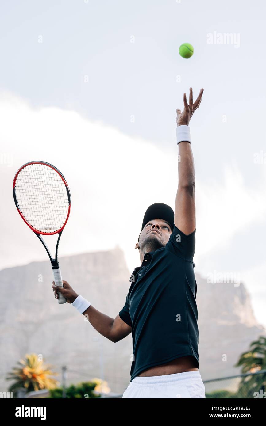 Tennis player throwing a ball in the air hitting a serve. Player is