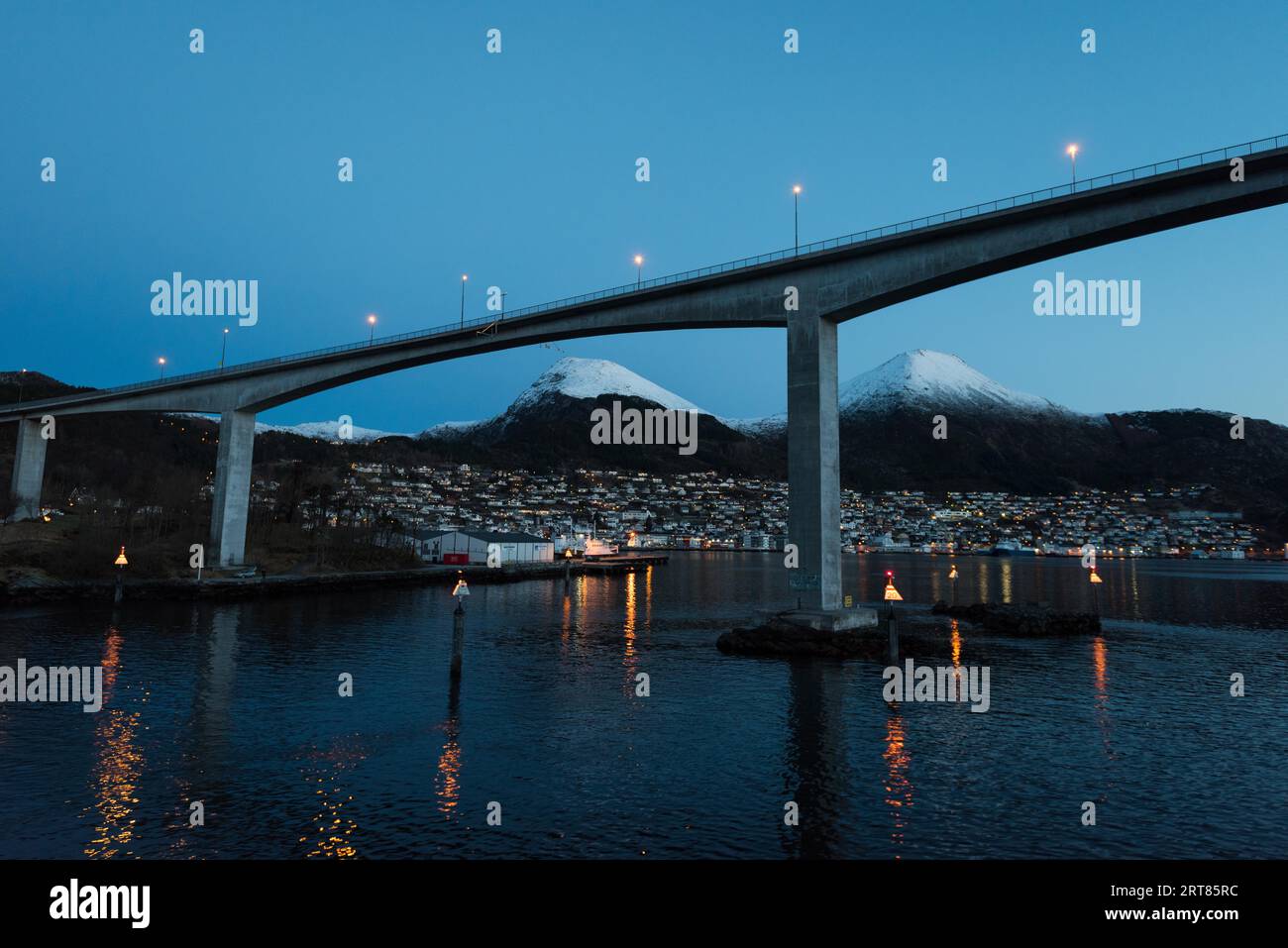 Bridge over fjord near the city Maloy in Norway seen from cruise ship in early morning with snow capped mountains on clear winter day Stock Photo