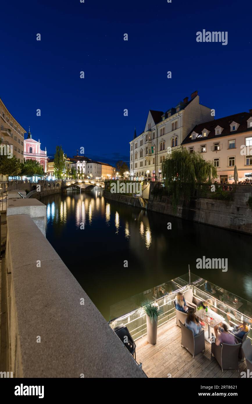 The promenade above a restaurant terrace on the Ljubljanica river in the slovenian capital city Ljubljana with the Triple bridge and famous pink Stock Photo