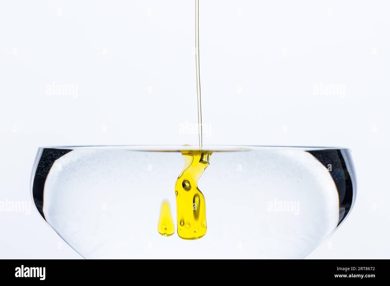 Detail of dash of olive oil drops gliding into glass of water isolated