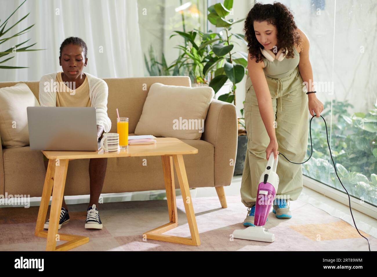 College student working on laptop when her roommate vacuum cleaning