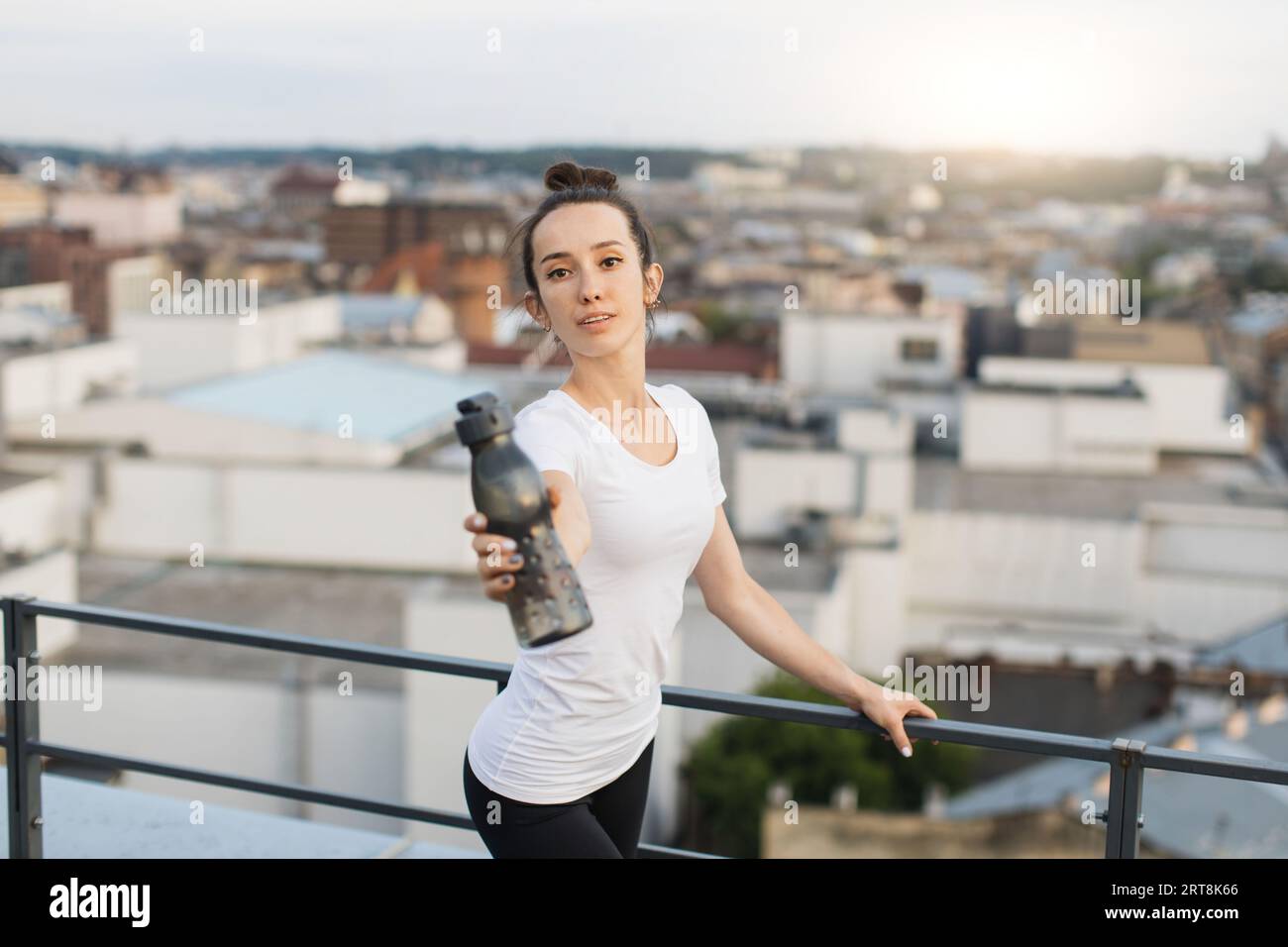 Lady in activewear reaching out sports bottle on roof Stock Photo