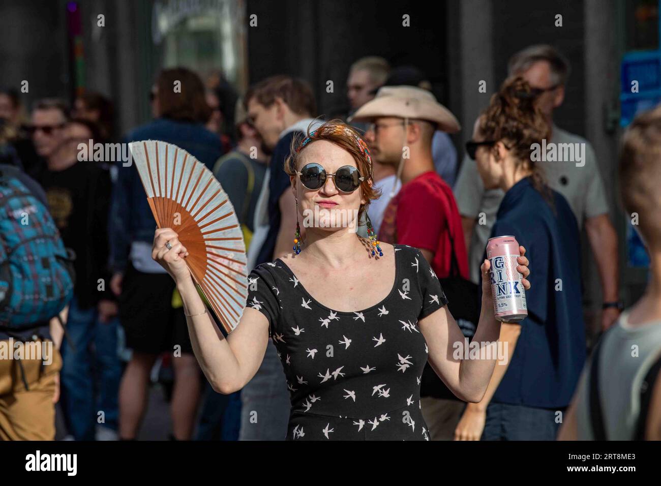 Woman with a handheld fan and a drink can at Kallio Block Party 2023 in Helsinki, Finland Stock Photo