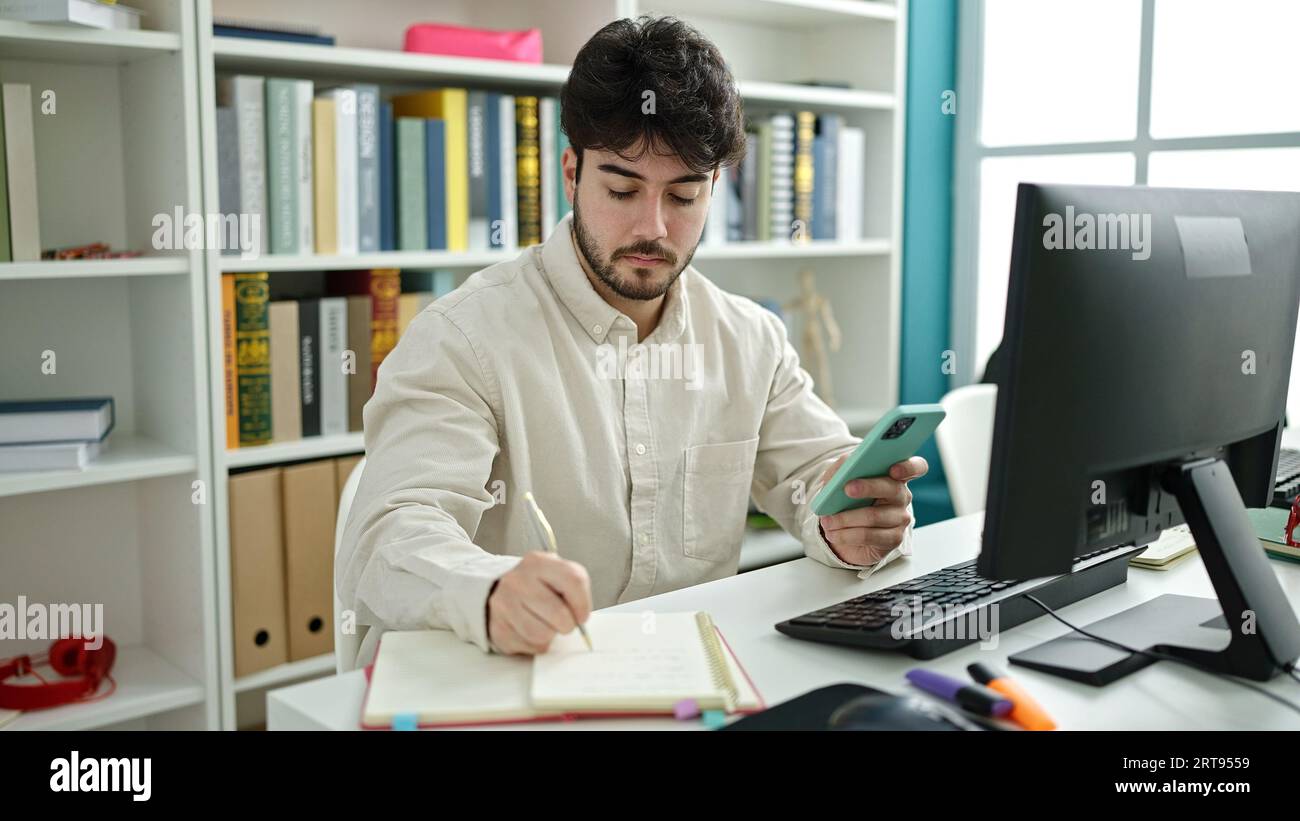 Young hispanic man student using computer and smartphone writing notes ...