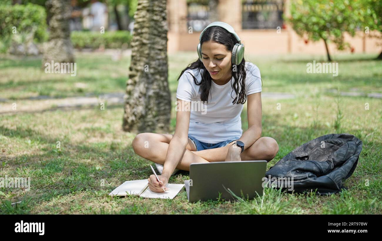 African american woman student using laptop and headphones taking notes ...