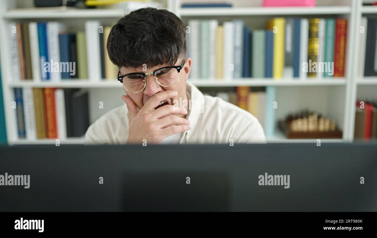 Young hispanic man student tired using computer yawning at library university Stock Photo