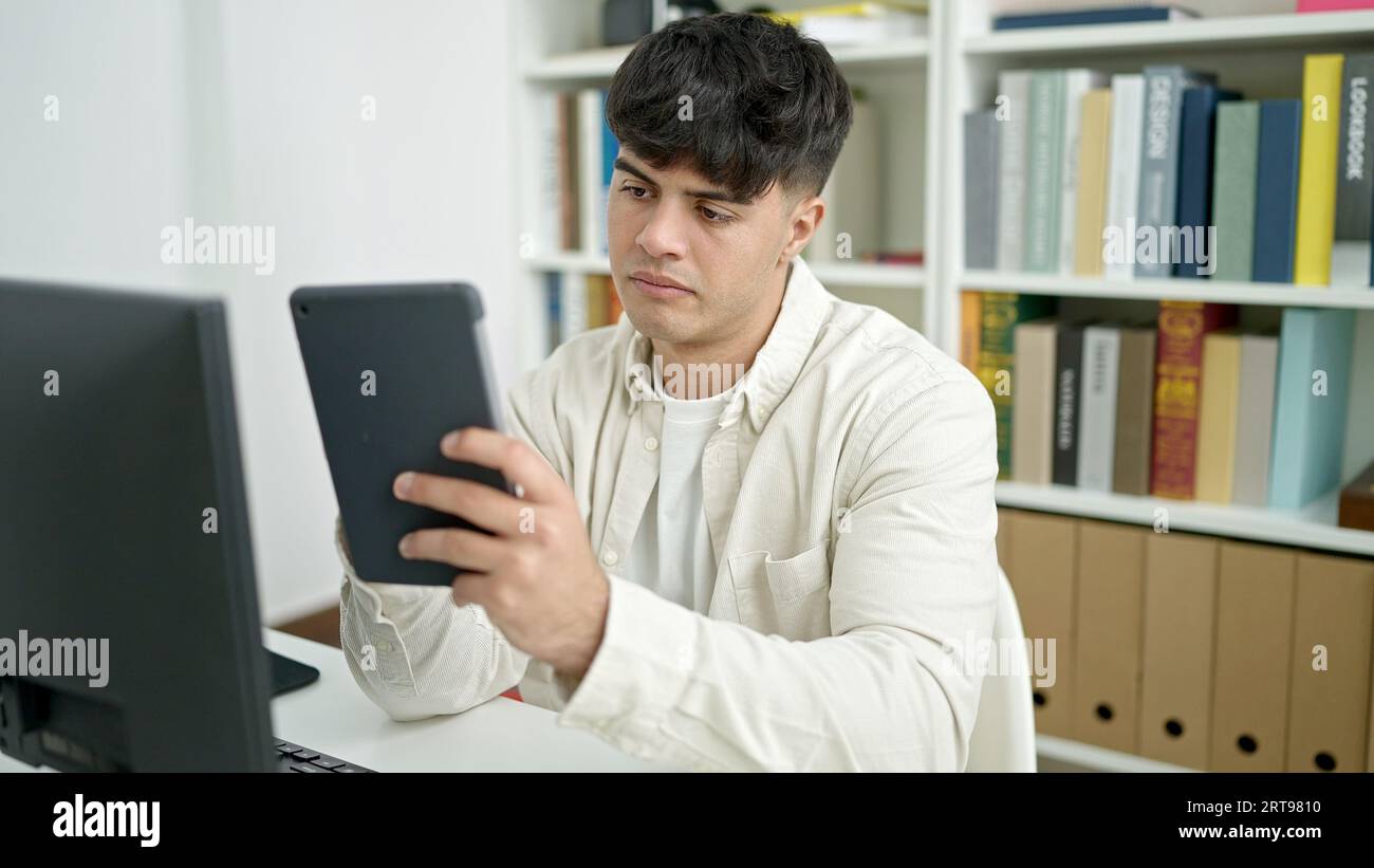 Young hispanic man student using computer and touchpad studying at ...