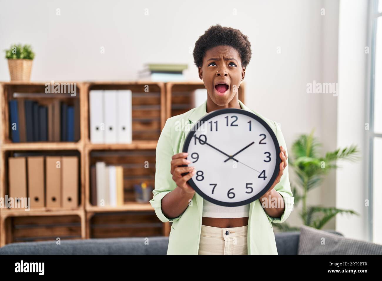 African american woman holding big clock angry and mad screaming ...