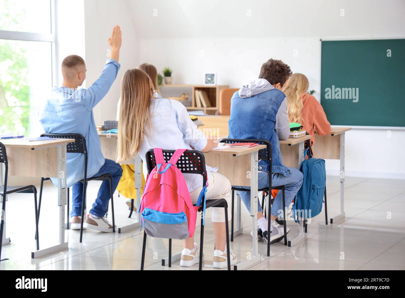 Male student raising hand to answer with his classmates in classroom Stock Photo