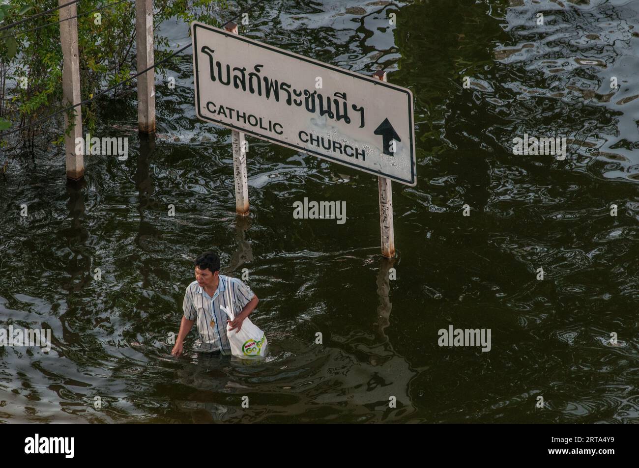 Thai man wades down flooded street past a bilingual directional sign in Rangsit, a Northern Suburb of Bangkok, Thailand. November, 2011. © Kraig Lieb Stock Photo