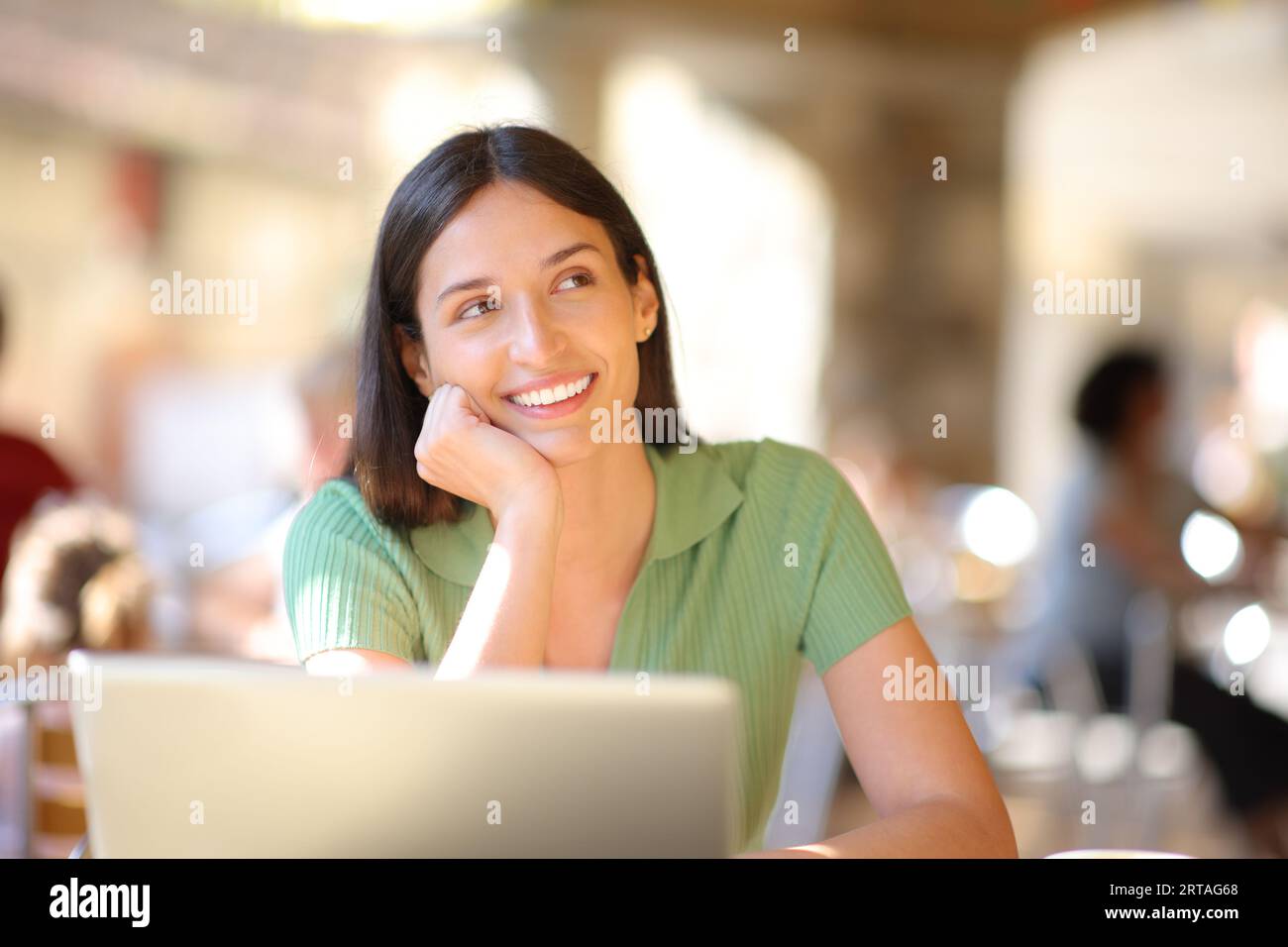 Happy woman with laptop thinking in a restaurant terrace looking at side Stock Photo