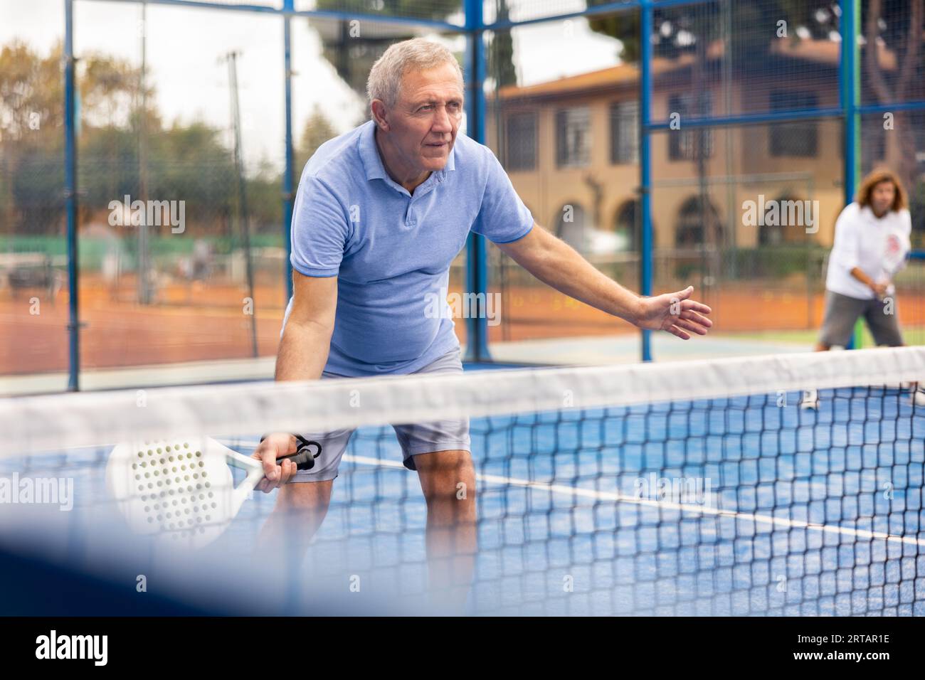 European old man holding padel racquet in hand and ready to return ball ...
