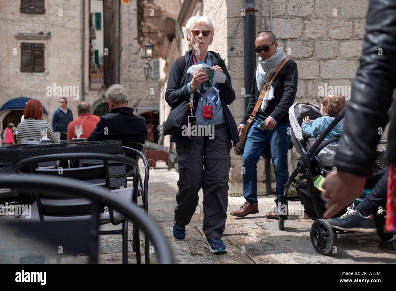 Kotor, Montenegro, Apr 17, 2023: Elderly lady snacking and walking down the narrow cobblestone street of Old Town Stock Photo