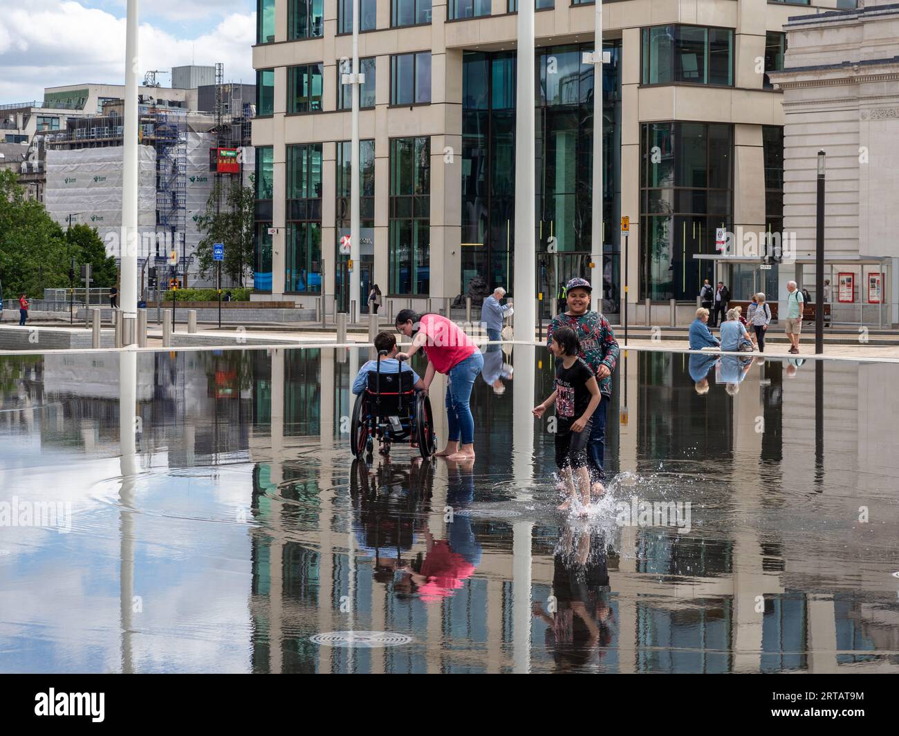 Visitors to Birmingham UK cool down in a shallow pool in Centenary Square, on a warm summer day; England, UK Stock Photo
