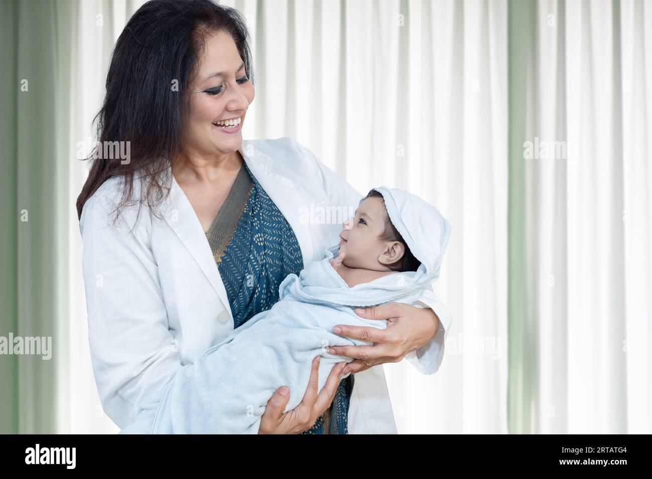 Young indian female doctor or nurse holding newborn baby wrapped in blanket. Portrait of medical worker with infant kid in hospital ward. Stock Photo