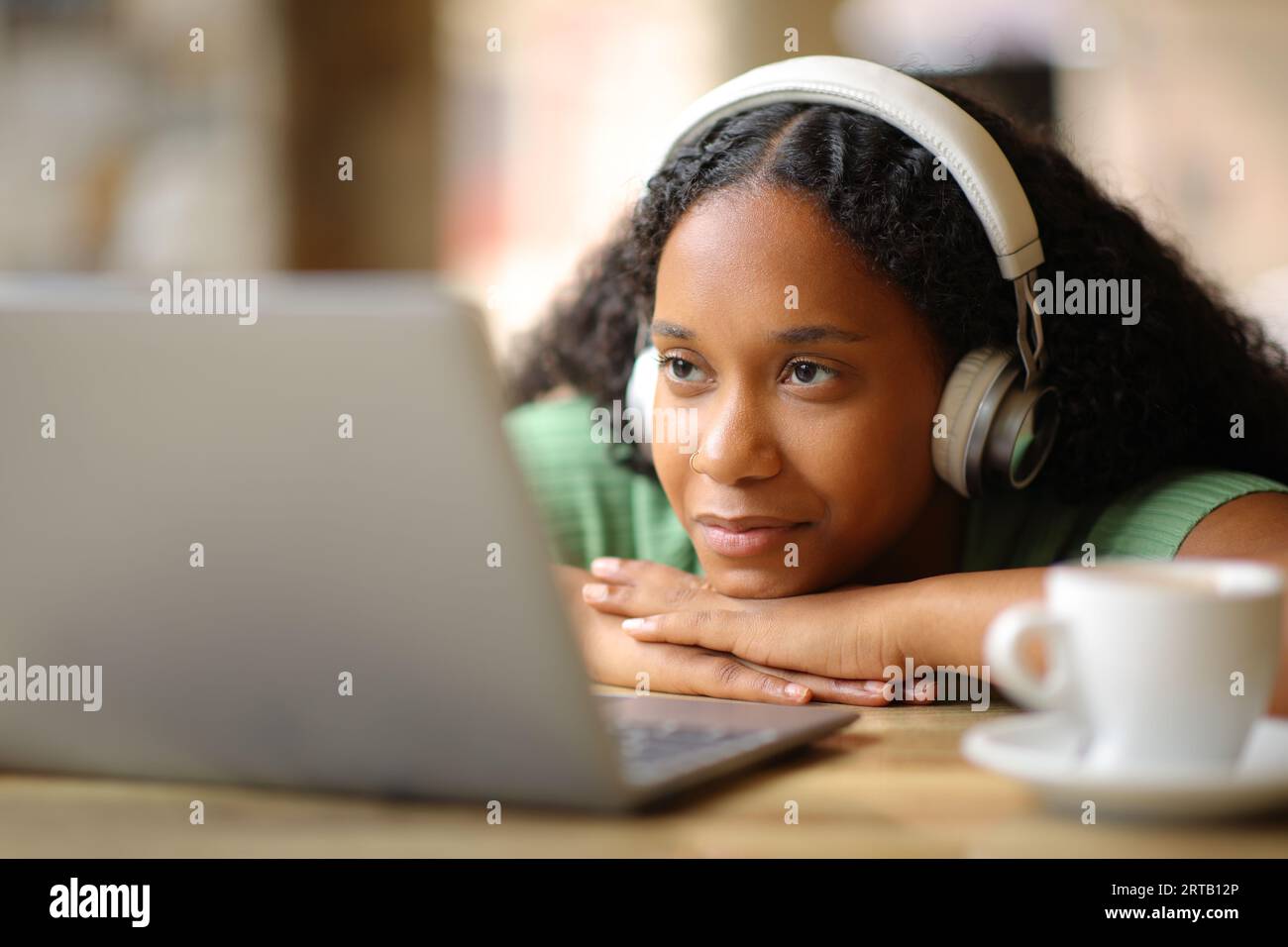 Black woman wearing headphone watching media on laptop in a restaurant terrace Stock Photo