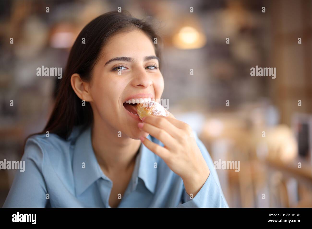 Happy bar customer looking at you eating croissant in a coffee shop