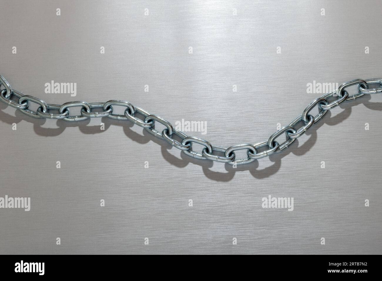 Top view of handmade customized reflecting link metal chain with shadow placed in zigzag shape on silver background in glowing light Stock Photo