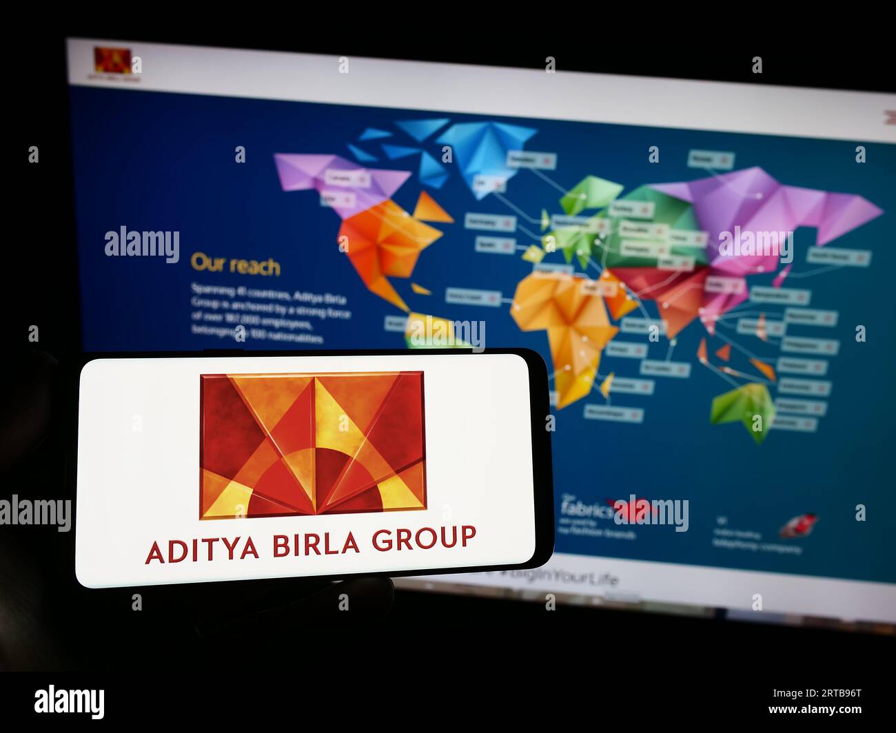 Person holding smartphone with logo of Indian company Aditya Birla Group (ABG) on screen in front of website. Focus on phone display. Stock Photo