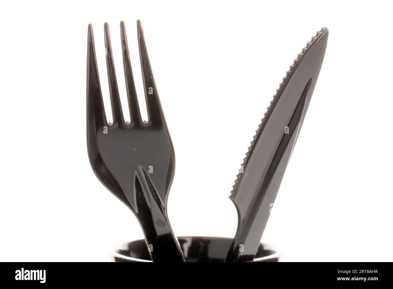 One plastic knife and fork in a black ceramic cup, macro, isolated on