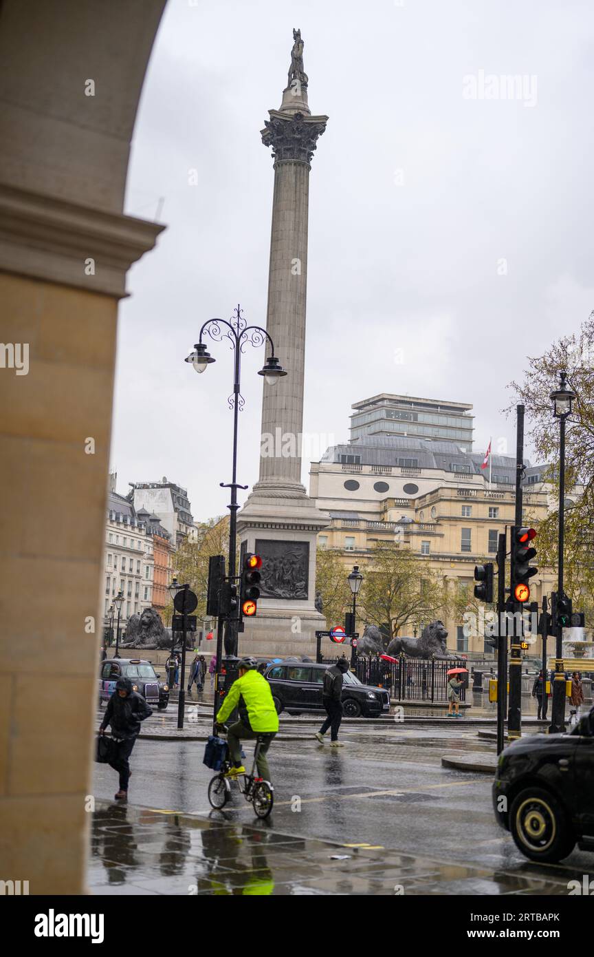 LONDON - April 24, 2023: Pedestrians, cyclists, and cars navigate a rainy day in the heart of Trafalgar Square, capturing the essence of British urban Stock Photo