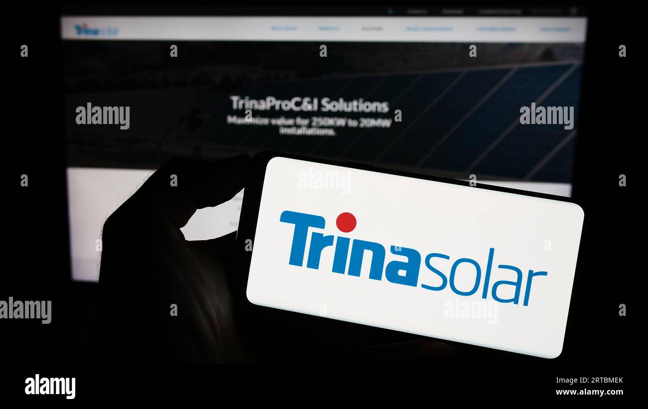 Person holding smartphone with logo of Chinese PV company Trina Solar Co. Ltd. on screen in front of website. Focus on phone display. Stock Photo