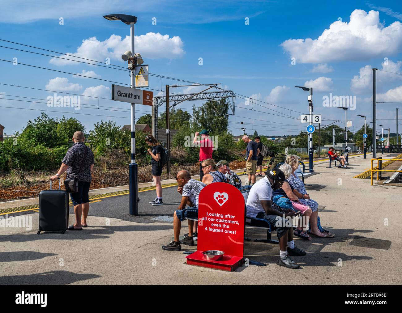 Grantham, Lincolnshire, UK – Passengers and travellers waiting in the sunshine on the platform for a train Stock Photo