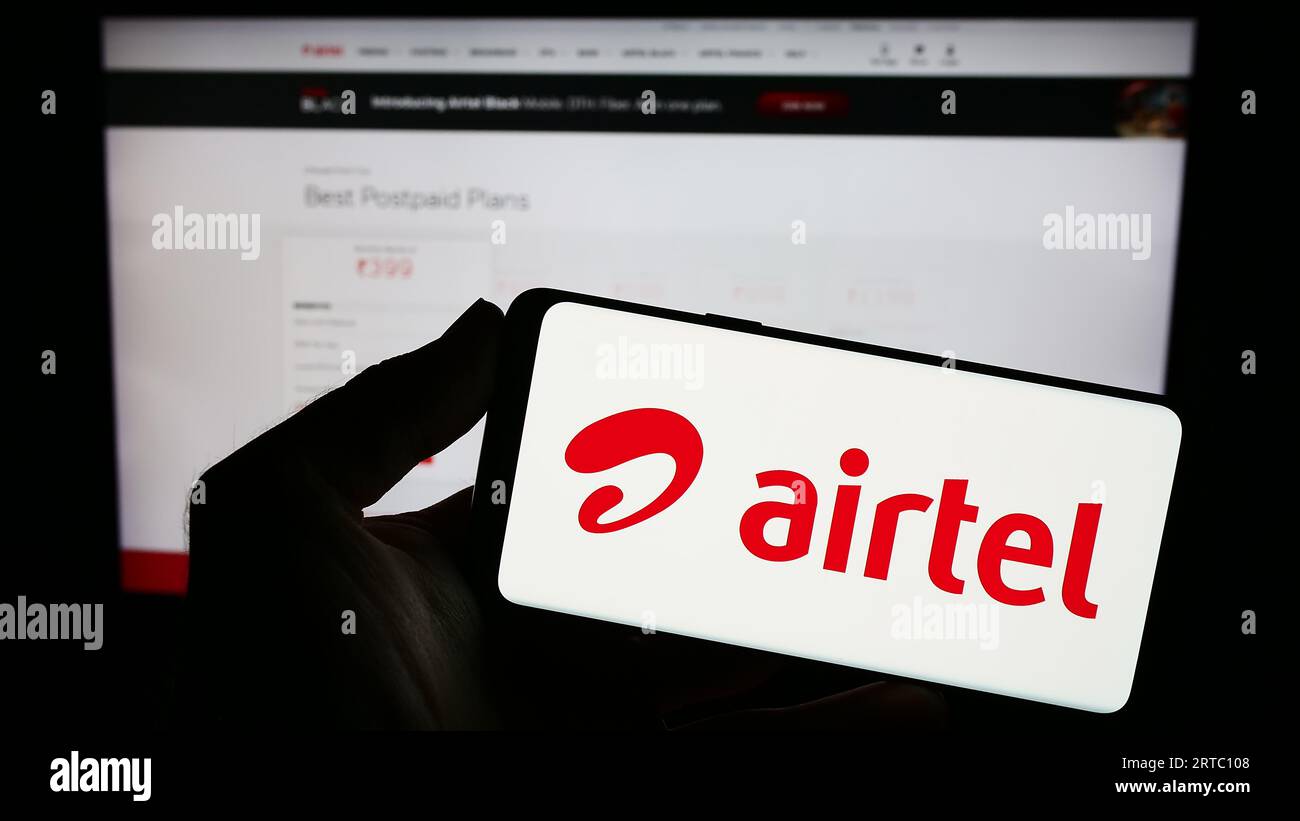 Person holding smartphone with logo of telecommunications company Bharti Airtel Limited on screen in front of website. Focus on phone display. Stock Photo